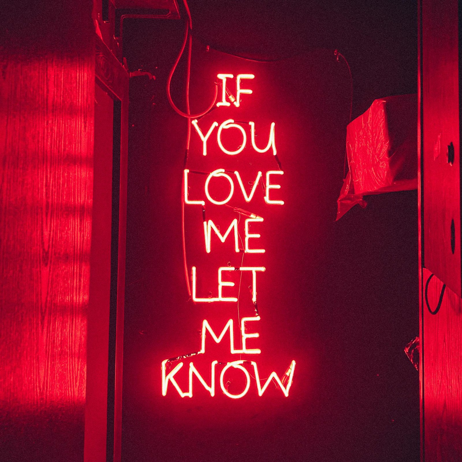 pexels-photo-11811929-11811929 Vibrant red neon sign with the text 'If you love me let me know' illuminated in a dark room setting.